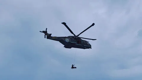 Low angle shot of rescue helicopter winching rescuer and stretcher basket Vídeo Stock 347687543
