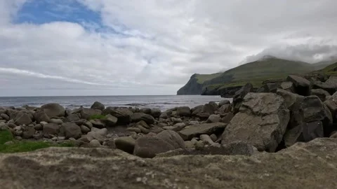 Low angle shot of rocky beach and misty cliffs in Sandur, Faroe Islands Stock Footage 339940981
