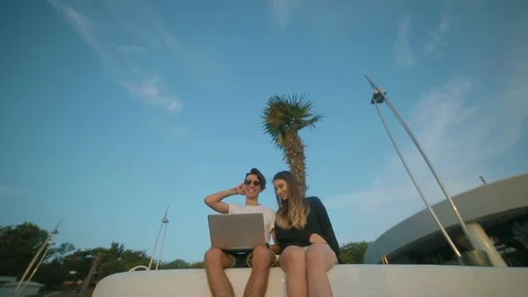 Low angle shot romantic couple sits on parapet with laptop Vidéo 102815525
