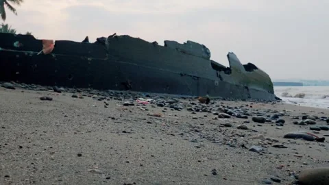 Low-angle shot of a rusted black shipwreck hull stranded on a rocky sandy beach Stock Footage 337776596