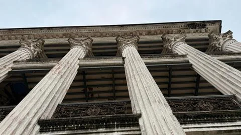 Low angle shot showcasing weathered columns and ornate iron balcony on an old Фото