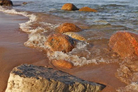 Low Angle Shot of Small Waves Rolling into Beach Dotted with Colorful Rocks and Foto stock