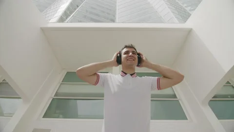 Low angle shot of a smiling, handsome teenager wearing wireless headphones Video stock 235393196