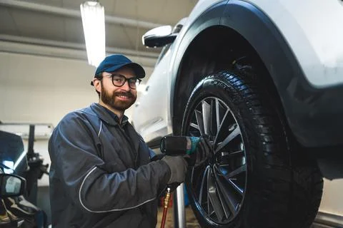 Low-angle shot of a smiling mechnic screwing a car wheel. Repair shop concept. Stock Photos