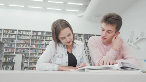 Low angle shot of two college friends studying together in a bright library Stock Footage 311985406