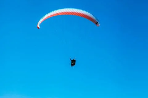 A low angle shot of two people flying a paraplane with clear blue sky in the  写真素材