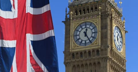 Low-angle shot of the Union Jack flag blowing in the wind beside Big Ben Stock Footage 319793140