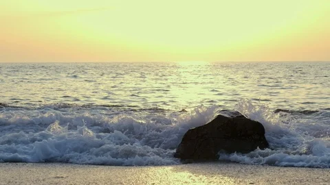 Low angle shot, waves splashing over boulder on beach in slow motion at sunset Stock Footage 115995609