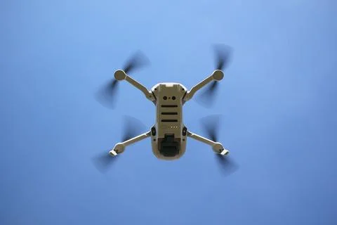 Low angle shot of a white drone with spinning propellers on a blue sky backgroun Foto stock