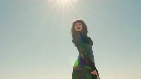 Low angle shot of a young Goth woman, with pale sky and sun flare Stock Footage 293117283