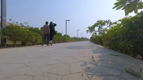 Low angle shot of a young indian couple walking on an empty road path in a garde Stock Footage 146033556