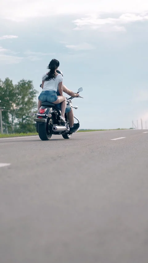 Low angle shot young man and woman ride black motorcycle Stock Footage 308000671