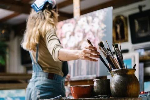 Low angle side view of female artist taking paintbrush from pot with various  Stock Photos