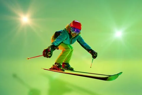 Low angle, side view of female athlete, skier in colorful gear mid-air jump neon Photos