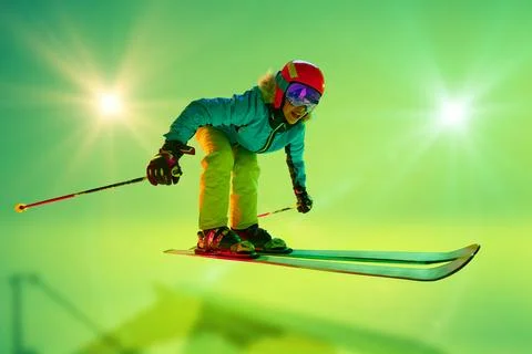 Low angle, side view of female athlete, skier in colorful gear mid-air jump neon 스톡 사진