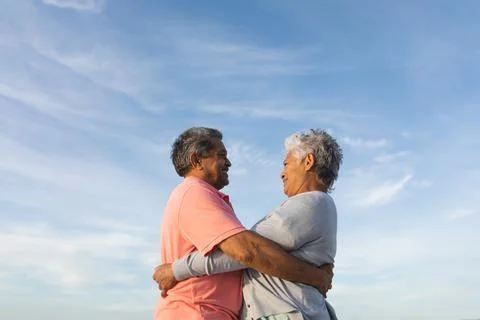 Low angle side view of smiling biracial senior couple looking while embracing Stock Photos