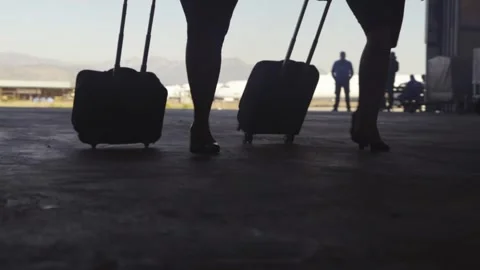Low angle silhouettes of aircrew walking through hangar with rolling suitcase Stock Footage 337419158