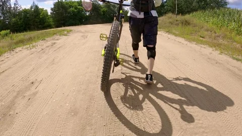 Low angle slow motion footage of a man walking on sandy road with his bicycle Stock Footage 159195110