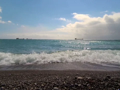 Low angle, slow motion hd video of sea waves on a pebble beach and ships Stock Footage 75513019