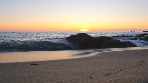 Low angle, slow motion shot of ocean waves breaking over rocks on sandy beach Stock Footage 115757554