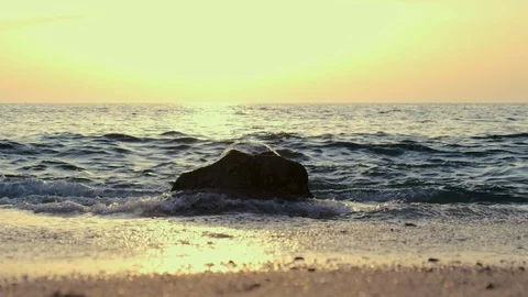 Low angle, slow motion shot on beach of wave splashing against rock on shore Stock Footage 115998211