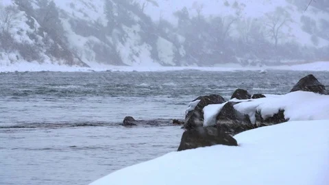 Low angle snow falling on Yellowstone River in Montana near bank Stock Footage 121064444