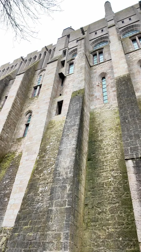 Low angle static shot of the Mont Saint-Michel Abbey towering over traditional s Vídeos de archivo 332724012