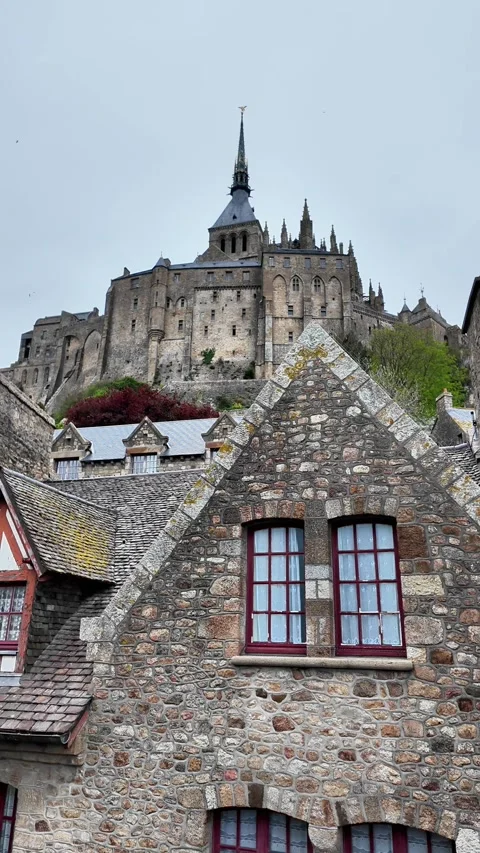 Low angle static shot of the Mont Saint-Michel Abbey towering over traditional s Vídeos de archivo 332724169