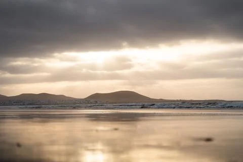 Low angle of sunset over calm ocean reflecting distant hills and cloudy sky Stock Photos