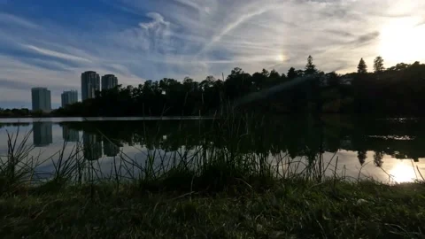 Low angle sunset pond ripples waves reeds foreground streaky clouds lens flare Stock Footage 215888767