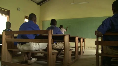 LOW ANGLE:  TEACHER WRITING ON BLACKBOARD, ADDRESSING STUDENTS AT WOODEN DESKS Stock Footage 60116268