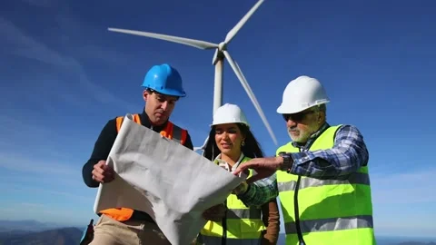 Low angle of three multiethnic engineers discussing plans for wind turbine .. Stock Footage 294975826
