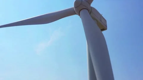 Low angle tilt shot of a spinning wind turbine against clear blue sky Video stock 335952425