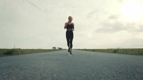 Low Angle Tracking Shot of a Female Athlete Running down the Empty Road Видео 133255737