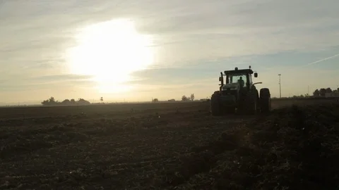 Low-angle Tractor drives across Sun pulling Plow Chisel. Stock Footage 94642895