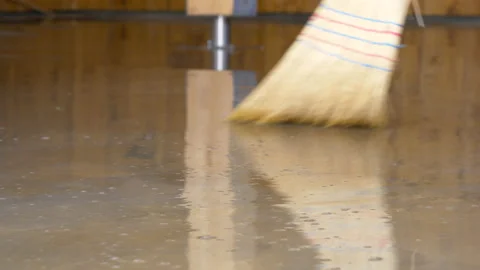 LOW ANGLE: Unrecognizable person uses a straw broom to sweep the flooded floor. Stock Footage 167503100