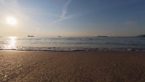 Low angle video of sun over calm sea with cargo ships on sandy beach horizon Vídeo Stock 347641412