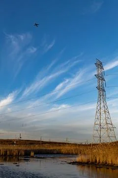 Low angle view of an airplane against the blue and cloudy sky, electric pylons Stock Photos