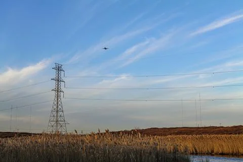 Low angle view of an airplane against the blue and cloudy sky, electric pylons Stock Photos