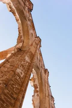 A low-angle view of ancient brick ruins with Gothic arches against a clear blue Stock Photos