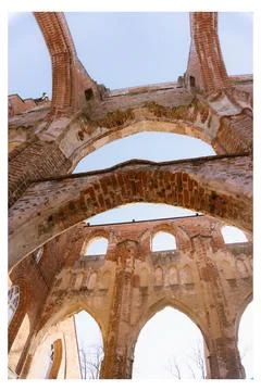 A low-angle view of ancient brick ruins with Gothic arches against a clear blue Stock Photos