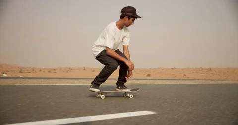 Low angle view of an Arab youth skateboarding on a desert road. Stock Footage 119570394
