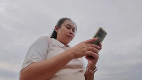 Low Angle View of Asian Woman Using Smartphone Against Sky Stockbeeldmateriaal 344098437