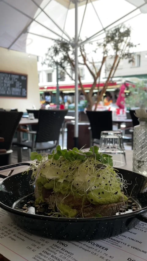 Low angle view of avocado toast on outdoor cafe table with blurred patio scene Stock Footage 341661795