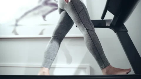 Low angle view of barefoot female in sportwear walking on electric treadmill in Stock Footage 134635303