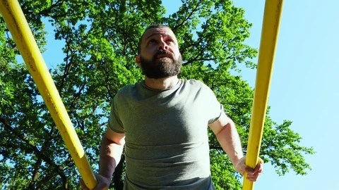 Low-angle view of a bearded man doing push-ups on parallel horizontal bars Stock Footage 90371726