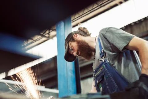 Low angle view of blue collar worker using welding machine in steel industry Fotos de archivo