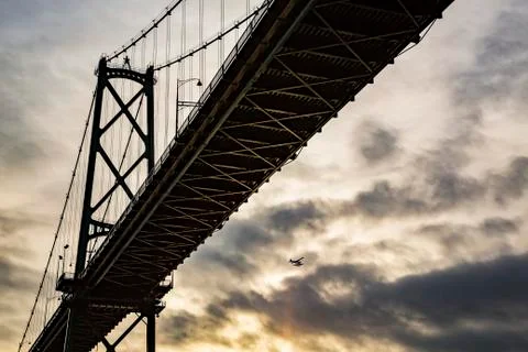 Low angle view of a bridge at sunset with an airplane flying in the distance Stock Photos
