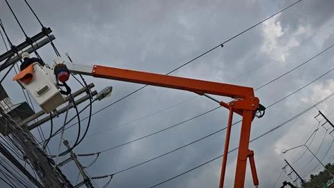 Low angle view of bright orange boom arm of bucket truck lifting lineman. Stock Photos