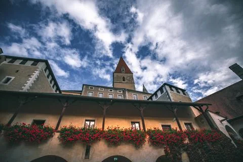 A low angle view of a building with a tall tower, red-tiled roof and red flowers Stock Photos